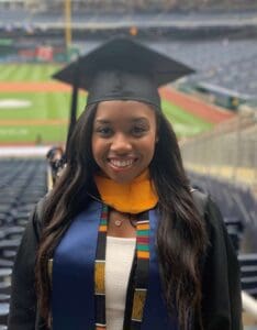 GRADUATE SUNDAY 2021 Alexis Jordan A woman in graduation gown and cap at a baseball game.