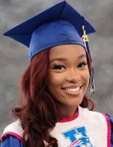 A woman in graduation gown and cap smiling.