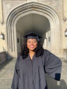 A woman in graduation cap and gown standing on the sidewalk.