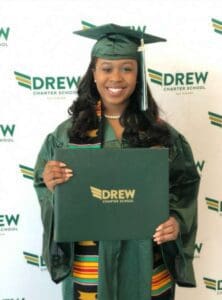 A woman in green cap and gown holding her diploma.