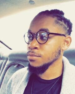 A man with glasses and a beard sitting in the back of a car.