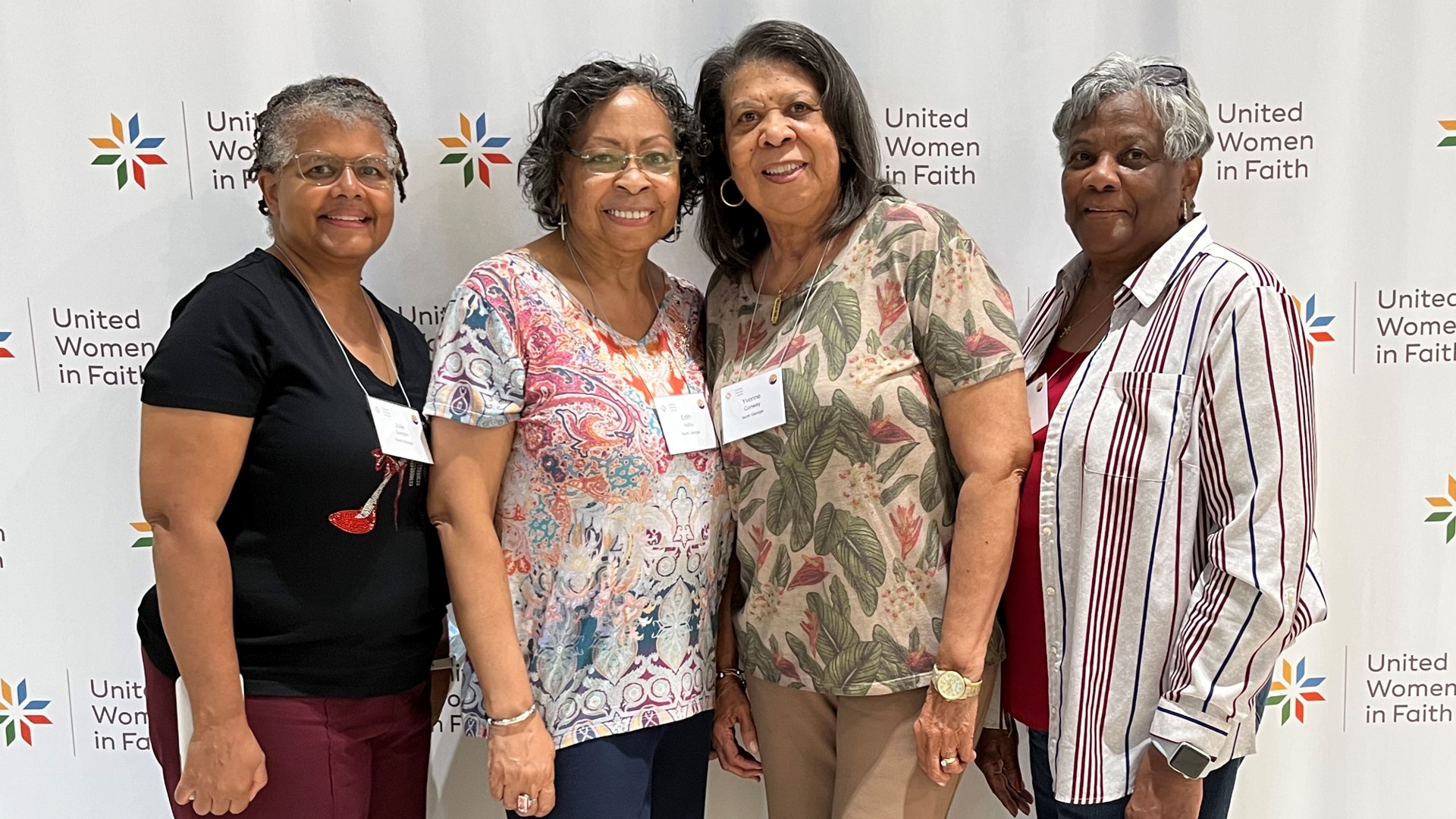 Four women standing next to each other in front of a white wall.