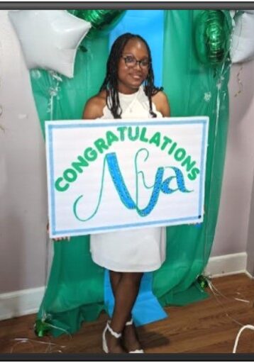 A girl holding up a sign that says congratulations mya.